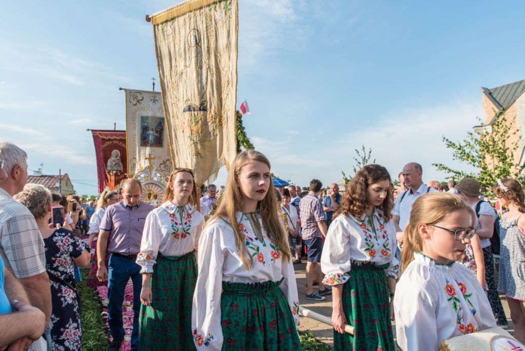 Grupa młodzieży podczas procesji. Na pierwszym planie dziewczyny w zielonych spódnicach w kwiaty i białe bluzki z haftem