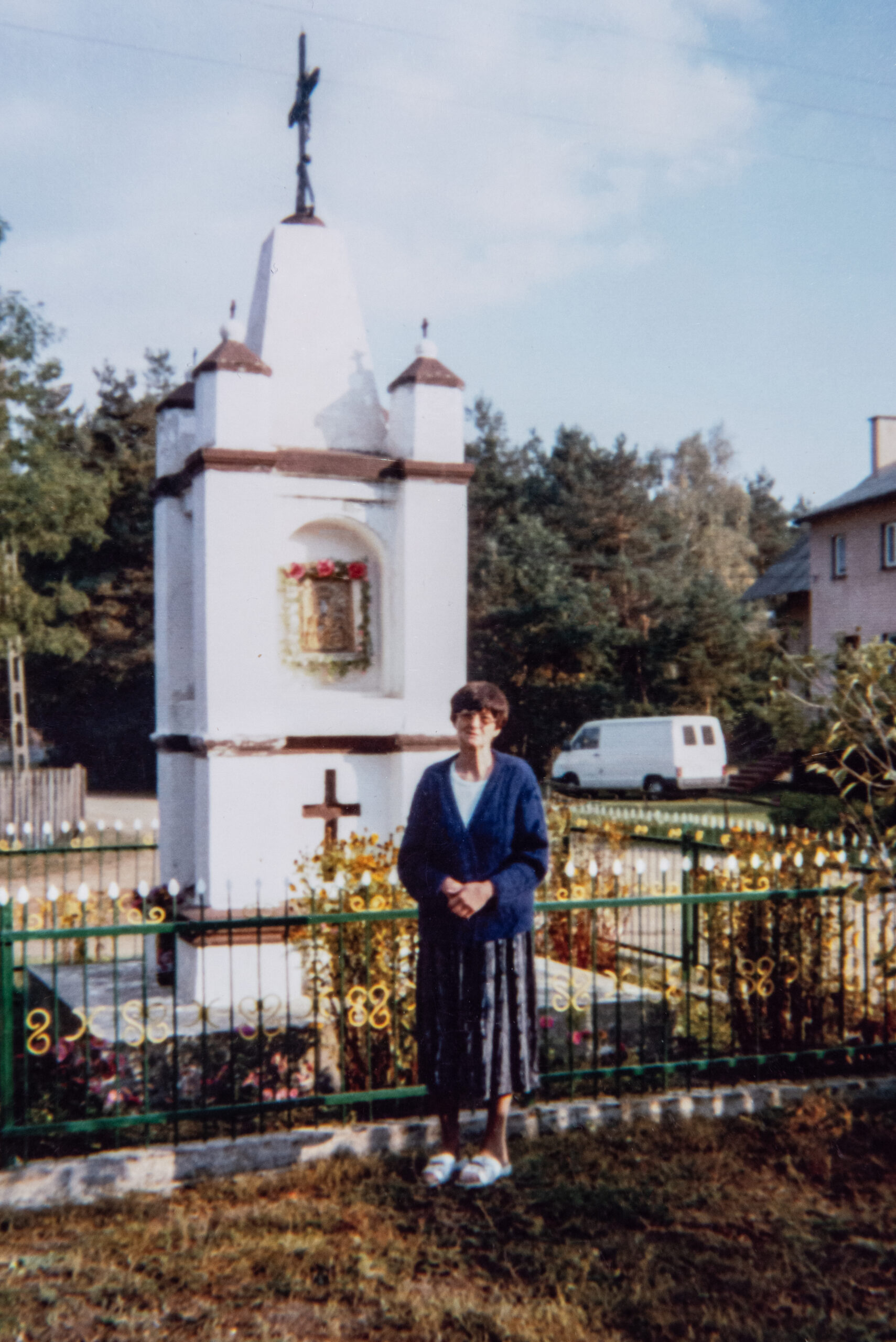 Kobieta w średnim wieku pozująca na dla białej zabytkowej kapliczki w Spycimierzu